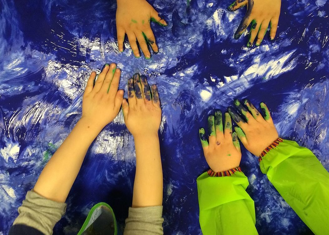 Grafika przedstawia ręce dzieci ubrudzone kolorowymi farbkami.